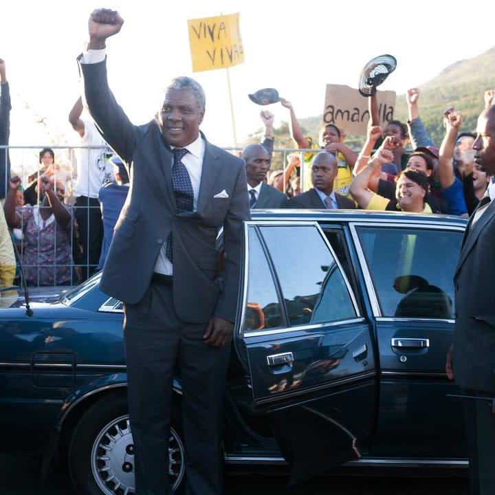 Idris Elba as Nelson Mandela stands next to a car with his fist in the air