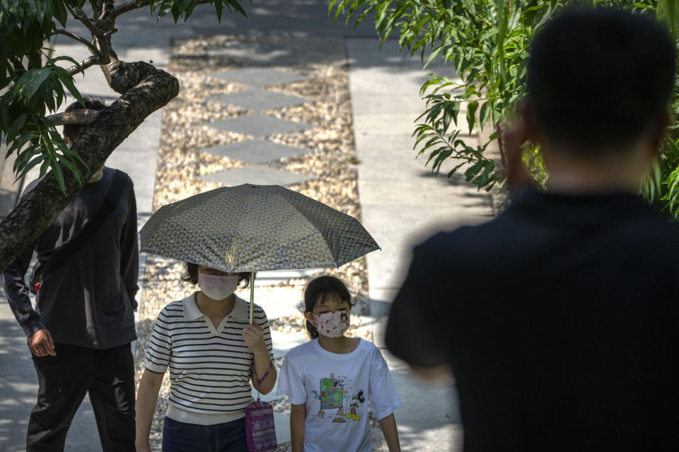 A woman and child wearing face masks walk along a path at a public park in Beijing, Tuesday, Aug. 30, 2022. (AP Photo/Mark Schiefelbein)