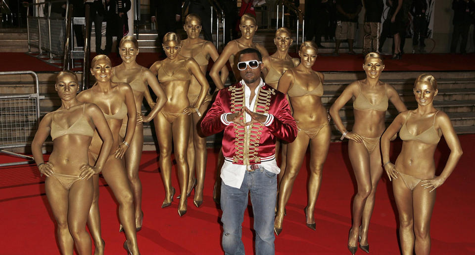 Kanye West at the BRIT Awards in 2006, flanked by bikini-clad women who are painted gold