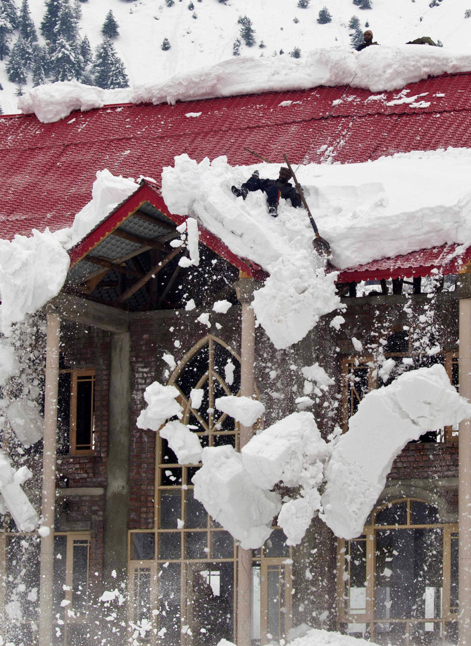 A Kashmiri villager slips as he clears snow off the roof of his house, which is under construction, in Gagangeri, some 80 Kilometers (50 miles) northeast of Srinagar, India. Photo:AP