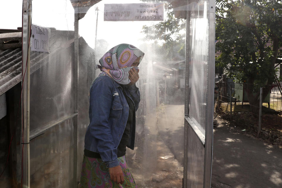 A woman covers her mouth as she is sprayed with disinfectant inside a makeshift sterilization booth set up outside a neighborhood during the coronavirus outbreak on the outskirts of Jakarta, Indonesia, Friday, April 3, 2020. The new coronavirus causes mild or moderate symptoms for most people, but for some, especially older adults and people with existing health problems, it can cause more severe illness or death. (AP Photo/Tatan Syuflana)