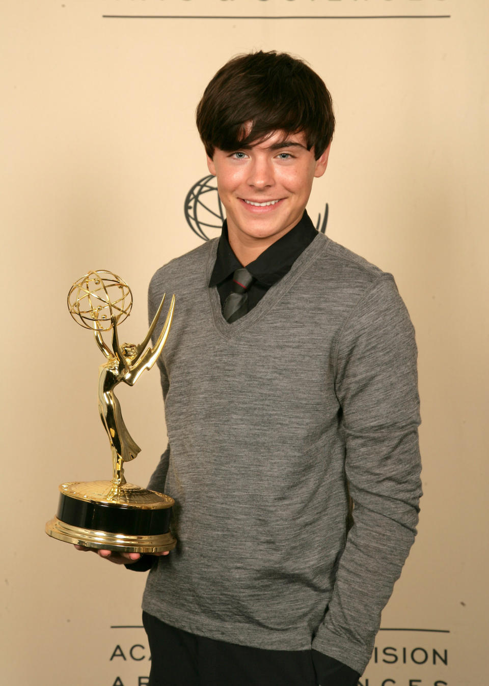 Zac in a long-sleeved sweater, holding an award