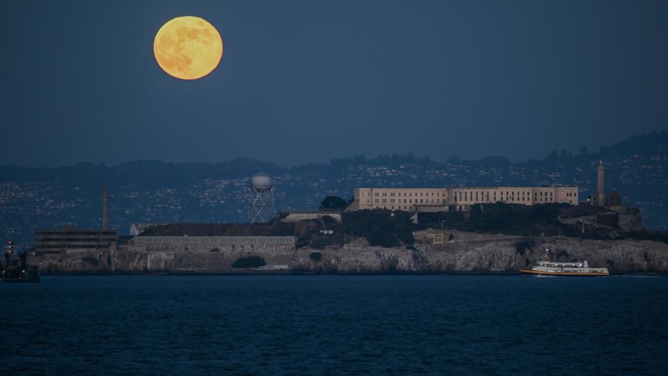 the full moon as seen over a rocky island in a bay