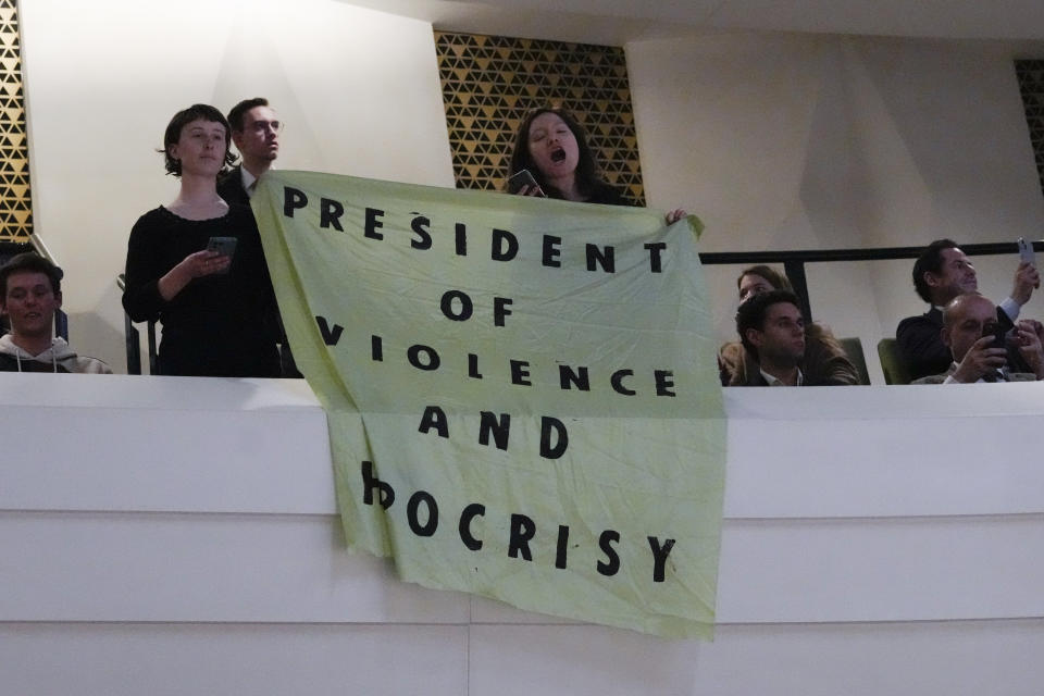 Demonstrator unfold a banner reading "President of Violence and Hypocrisy" as French President Emmanuel Macron explains his vision on the future of Europe during a lecture in a theatre in The Hague, Netherlands, Tuesday, April 11, 2023. (AP Photo/Peter Dejong)