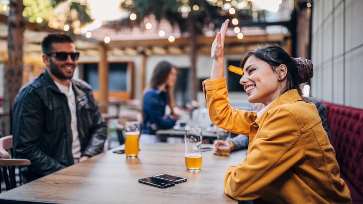  A man and a woman sitting outdoors at a bar, drinking beer together. 