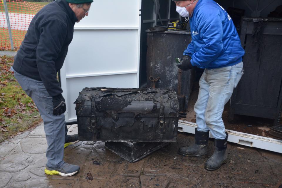 John Duckworth, left, and Timothy Burns look over a trunk that was damaged during the October fire at Stow Heritage House.