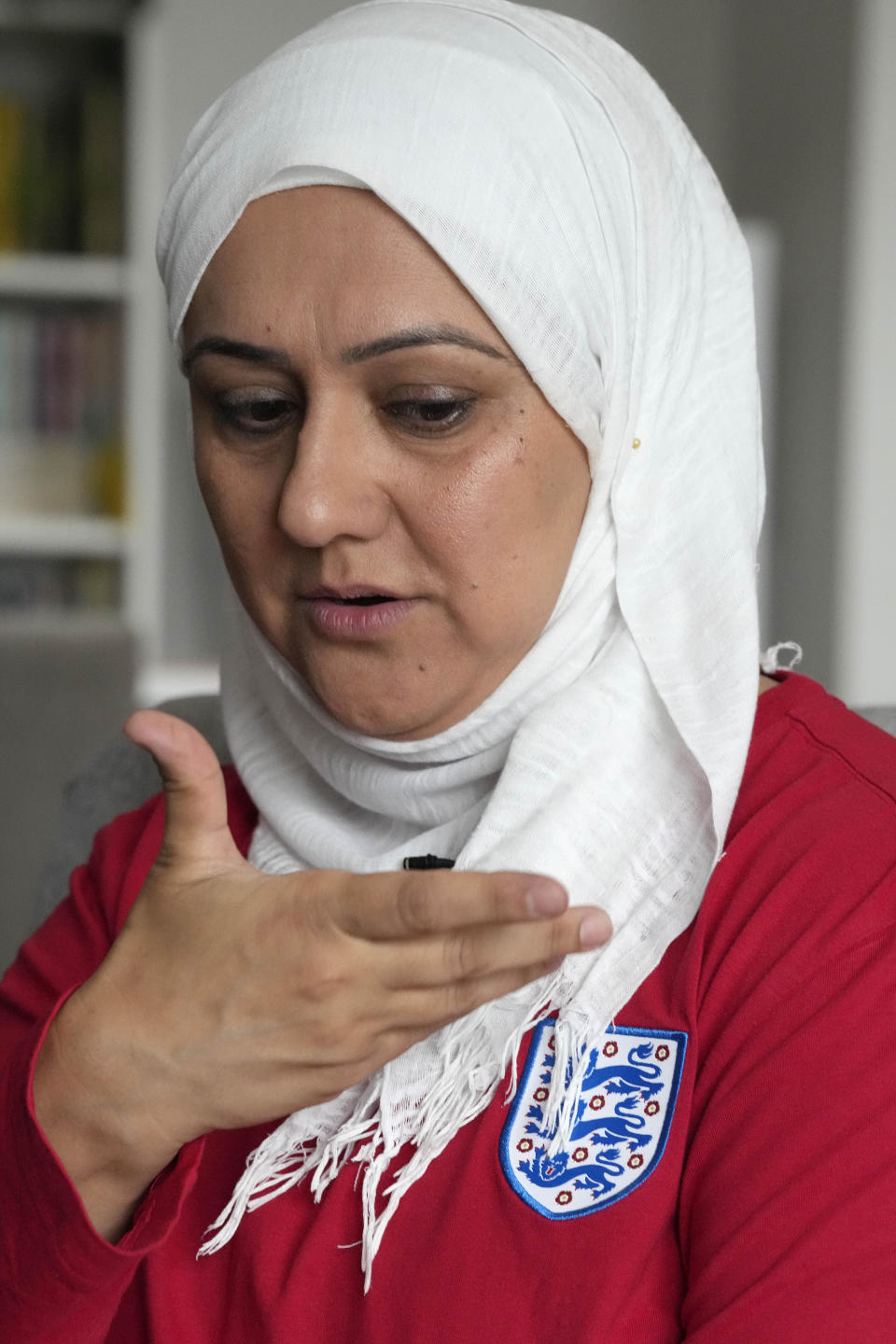 Huda Jawad points to the three lions emblem on her shirt as she speaks to The Associated Press, at her home in London, Friday, Aug. 18, 2023. Jawad is a member of a fan group known as the Three Hijabis for their traditional Muslim headscarves, a group that campaigns against discrimination in football. (AP Photo/Frank Augstein)