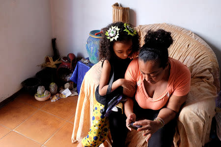 Anthonella Peralta looks at photos sent by her mother Yusmarlys Orozco, who lives in Dominican Republic, on grandmother Aura's phone, in their home in the slum Cota 905 in Caracas, Venezuela December 18, 2018. Picture taken December 18, 2018. REUTERS/Marco Bello