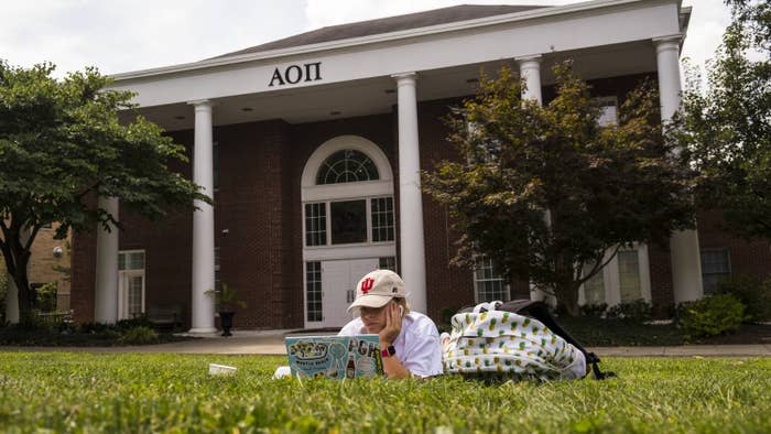 a student laying in the grass working on her laptop in front of a sorority house