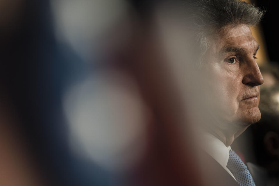 Sen. Joe Manchin, with a wary expression, listens at a news conference.