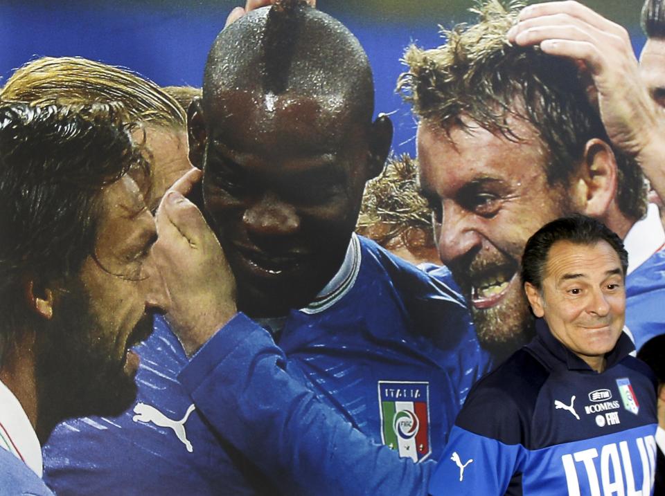 Italy coach Cesare Prandelli stands in front of a poster showing players, from left, Andrea Pirlo, Mario Balotelli, and Daniele De Rossi during a press conference at the national team's Coverciano training complex in Florence, Italy, Tuesday, April 15, 2014, where 42 players were called up for World Cup fitness tests. (AP Photo/Fabrizio Giovannozzi)