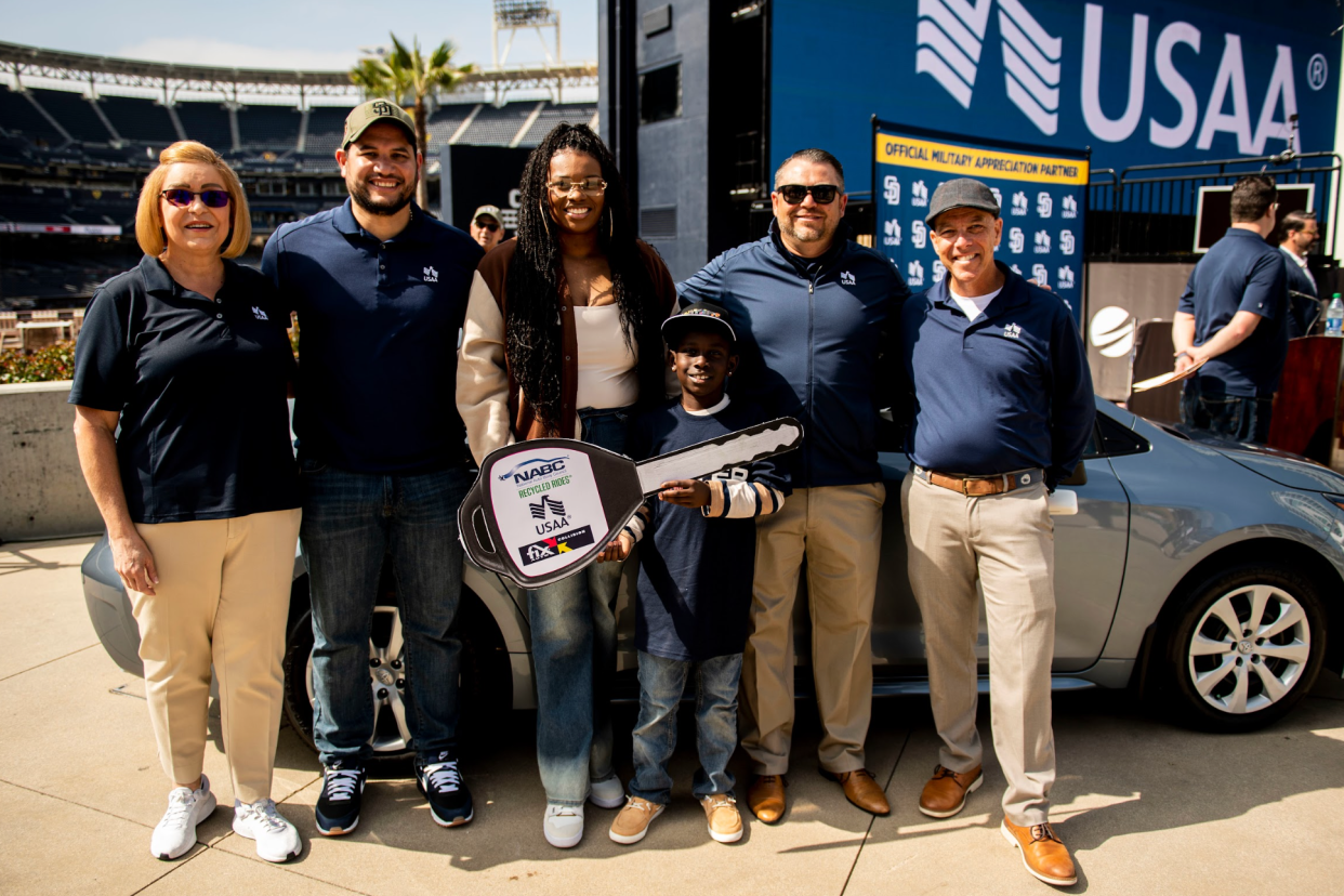 A woman holds a large key as a representative of the new car she was given by USAA