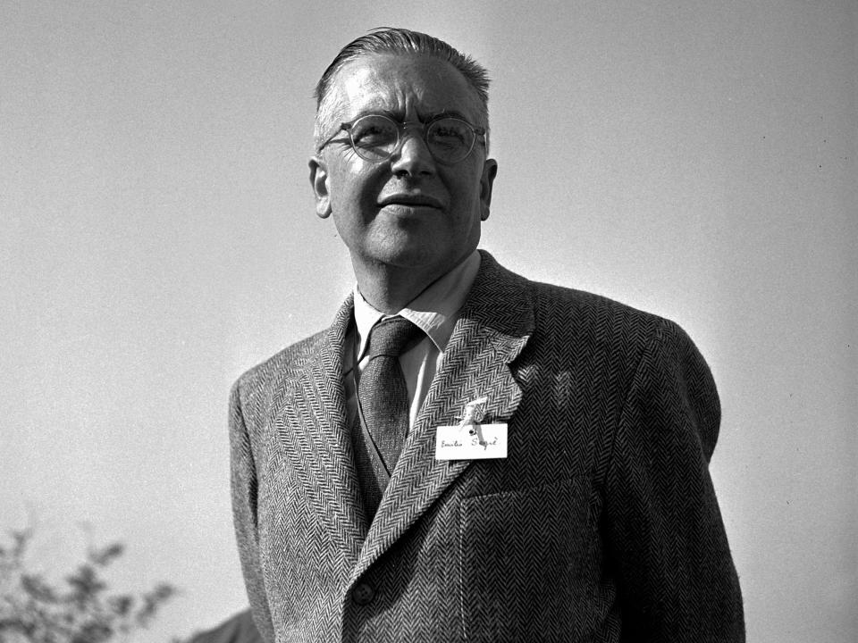 Nobel Prize winner Emilio Segrè stands outside wearing a suit with a corsage on the lapel in 1959
