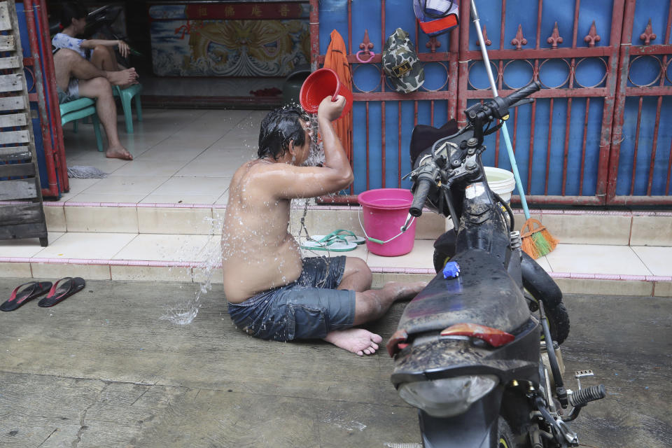 A man takes a shower in front of his flood-damaged house in Jakarta, Indonesia, Sunday, Jan. 5, 2020. Landslides and floods triggered by torrential downpours have left dozens of people dead in and around Indonesia's capital, as rescuers struggled to search for people apparently buried under tons of mud, officials said Saturday. (AP Photo/Tatan Syuflana)