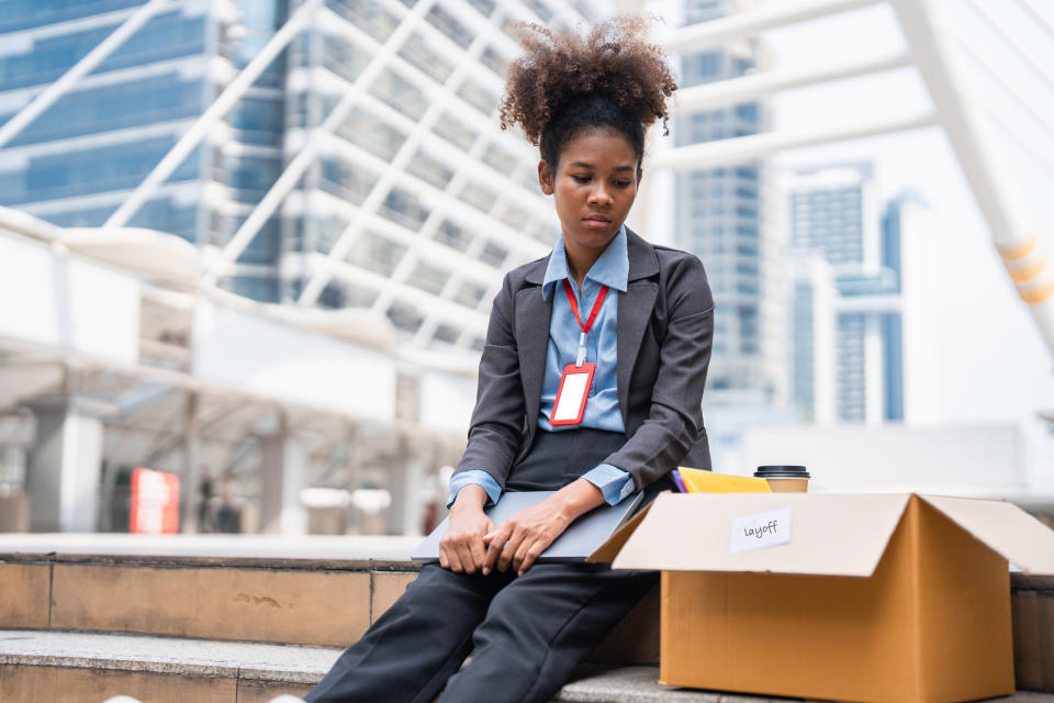 A woman looking sad next to a box of all her office belongings