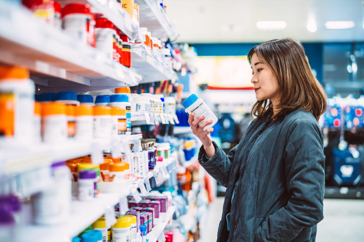 Beautiful Asian woman reading the ingredient label while shopping for multi vitamin & health supplements on shelf in supermarket. Heathy lifestyle concept.