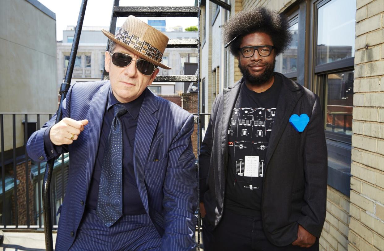 A white man and a Black man stand together by a metal staircase outdoors.