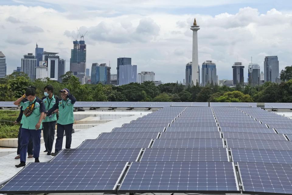 Workers walk near solar panels that provide partial electrical power to Istiqlal Mosque as the city skyline is seen in the background, in Jakarta, Indonesia, Wednesday, March 29, 2023. A major renovation in 2019 installed upwards of 500 solar panels on the mosque's expansive roof, now a major and clean source of Istiqlal's electricity. (AP Photo/Tatan Syuflana)