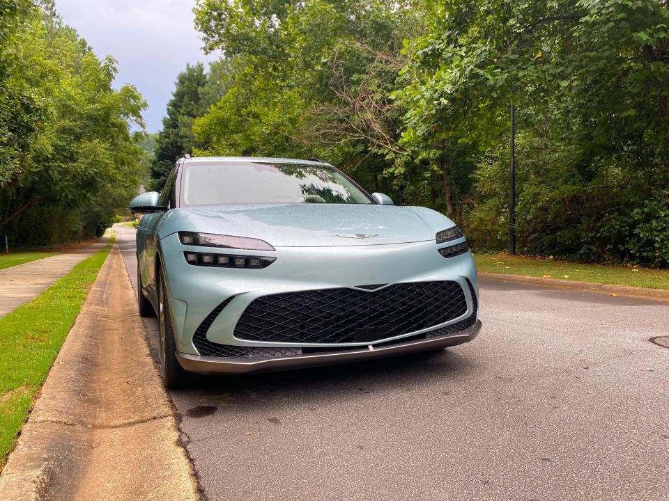 The left front of a green Genesis GV60 EV parked on the side of a street.