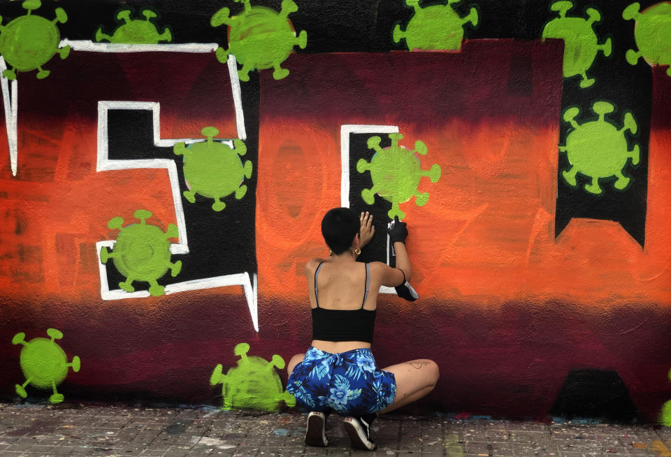 An artist sprays paints a wall with topic about the Coronavirus in Barcelona, Spain, Thursday, Aug. 13, 2020. Spain's daily number of new COVID-19 cases has shot up, with almost 2,935 officially reported Thursday compared with 1,690 the previous day. (AP Photo/Emilio Morenatti)