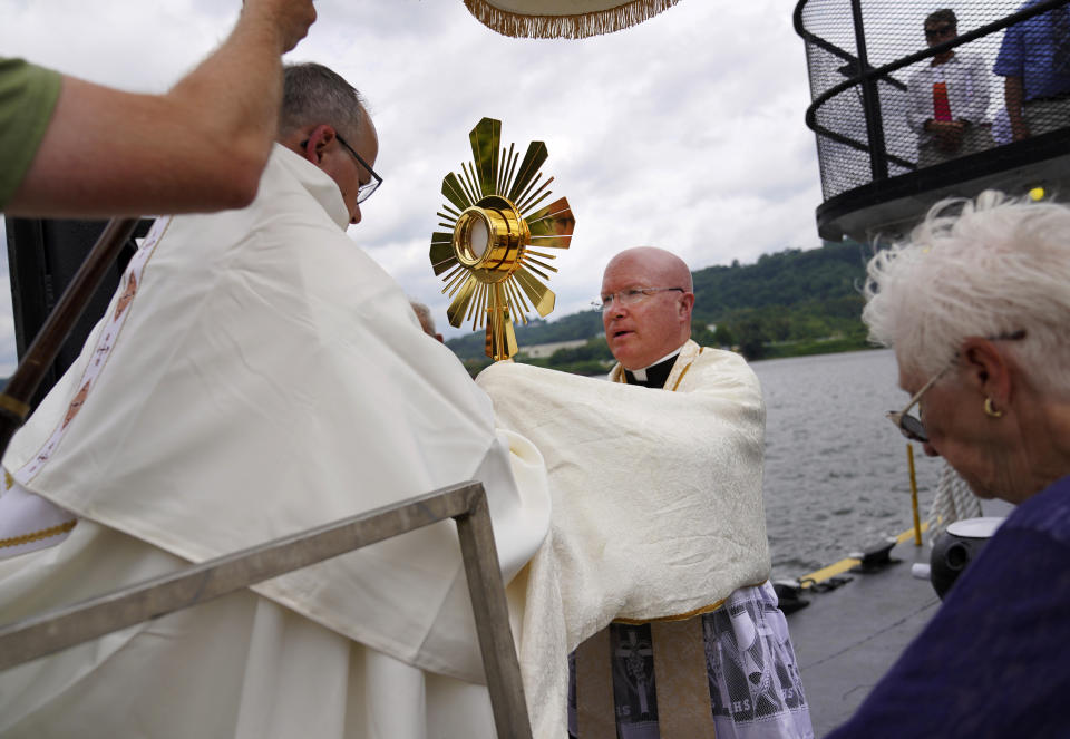 Bishop Edward Lohse, apostolic administrator of the Catholic Diocese of Steubenville, left, hands the Eucharist to the Rev. Roger Landry as they board a boat on the Ohio River as part of the National Eucharistic Pilgrimage, at the Steubenville Marina in Steubenville, Ohio, Sunday, June 23, 2024. (AP Photo/Jessie Wardarski)