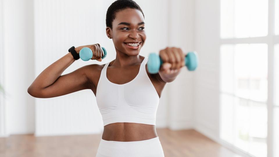 Woman holding two dumbbells punching forward with her left arm and holding her right hand above her shoulder