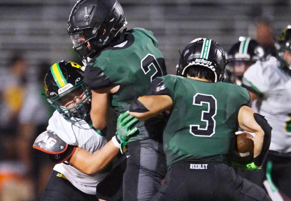 Malachi Ríos, de Redley, bloquea a Giovani Barrera de Roosevelt, izquierda, mientras Demetrius Vargas de Reedley, derecha, corre el balón, la noche del viernes 25 de agosto de 2023, en Reedley.