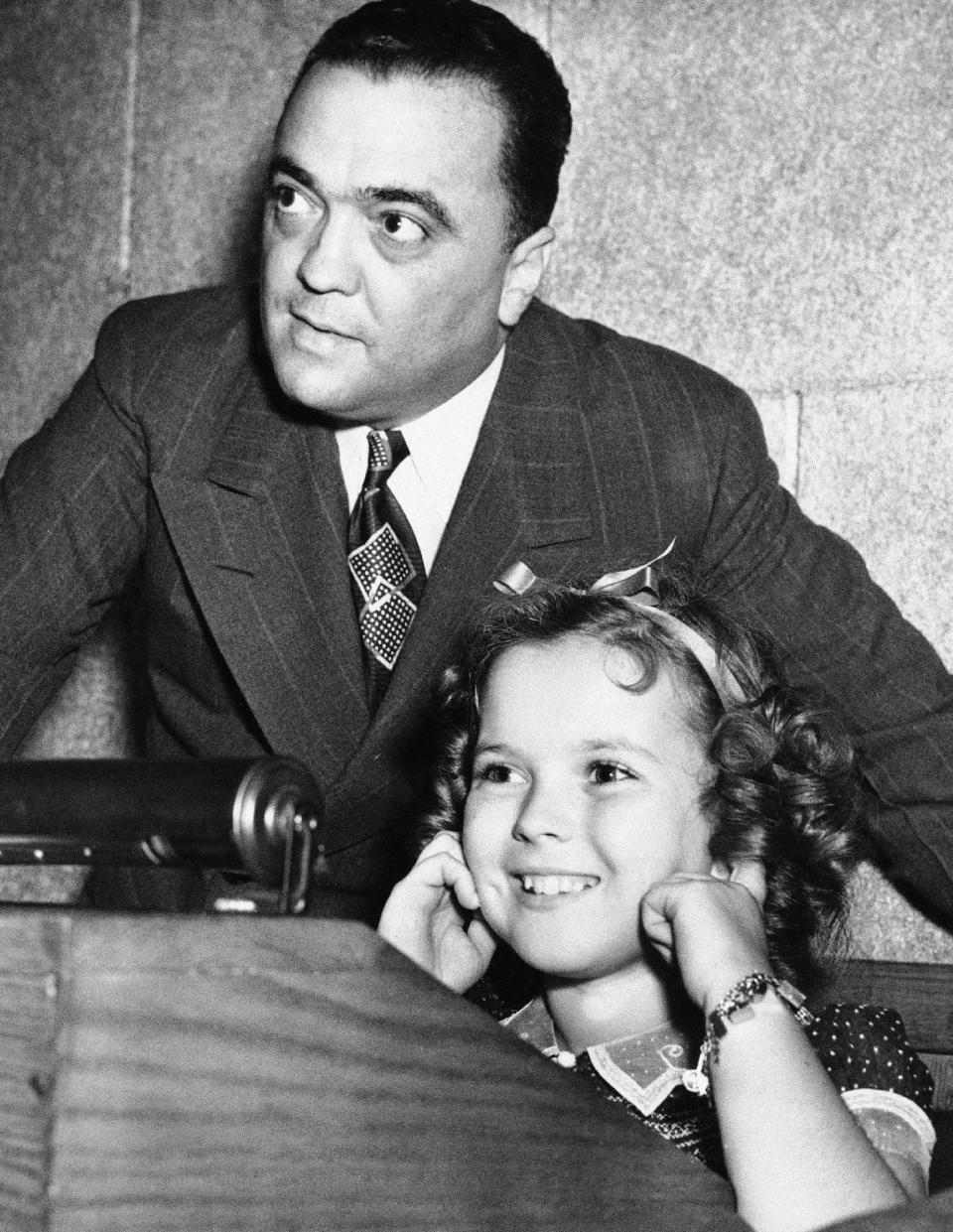 In this June 24, 1938, file photo, young actress Shirley Temple plugs her ears as her father shoots a federal agent's gun, while Federal Bureau of Investigation Director J. Edgar Hoover gives her a tour of FBI headquarters in Washington. Temple, who died at her home near San Francisco, Monday, Feb. 10, 2014, at 85, sang, danced, sobbed and grinned her way into the hearts of Depression-era moviegoers and remains the ultimate child star decades later. (AP Photo/File)