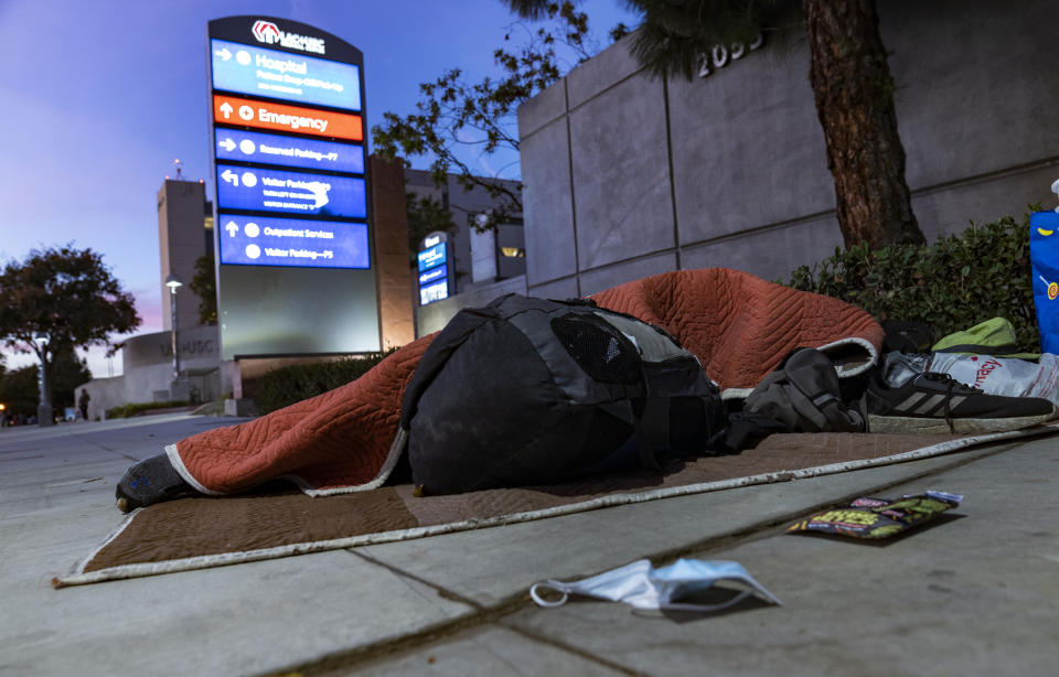 A homeless person sleeps outside the Los Angeles County+USC Medical Center hospital entrance in Los Angeles, late Wednesday, Dec. 16, 2020. The state has been grappling with soaring coronavirus cases and hospitalizations. Hospitals are filling up so fast that officials are rolling out mobile field facilities and scrambling to hire more doctors and nurses. (AP Photo/Damian Dovarganes)