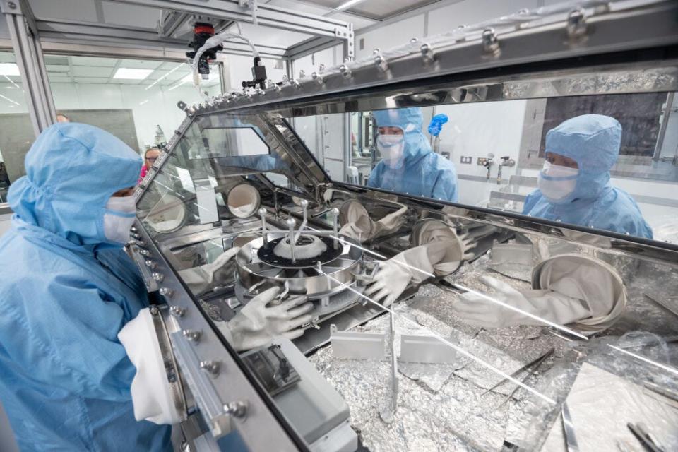 OSIRIS REx curation team pouring the sample from the TAGSAM head and examining sample material.