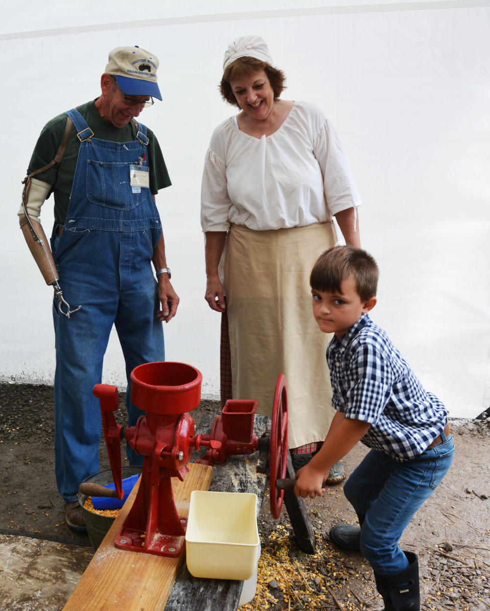 Gage Montgomery of Gray, tries his hand at cracking corn while Bill Blough and Gage's grandmother Wilma Horner offer guidance. Gage is going to feed his cracked corn to his chickens his grandmother said.