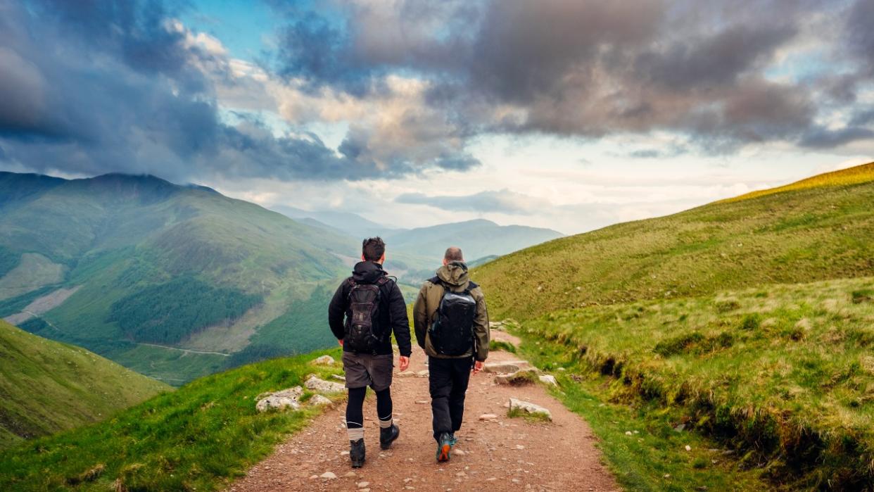  Two men pictured from the rear, walking along a hiking path on Ben Nevis in Scotland 