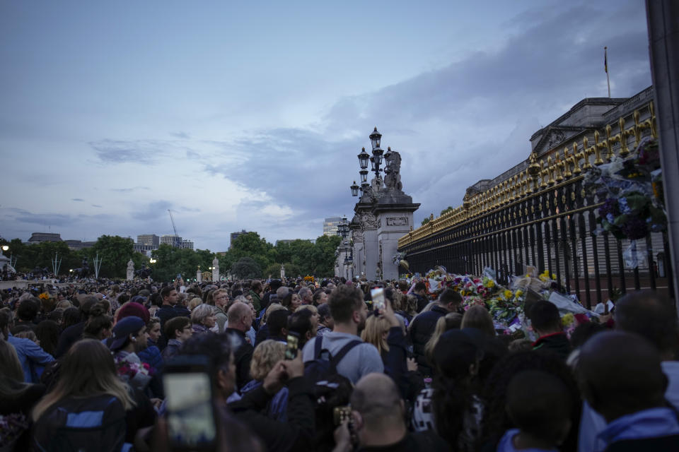 Mourners gather at dusk outside Buckingham Palace in London, Friday, Sept. 9, 2022. Queen Elizabeth II, Britain's longest-reigning monarch and a rock of stability across much of a turbulent century, died Thursday Sept. 8, 2022, after 70 years on the throne. She was 96. (AP Photo/Christophe Ena)