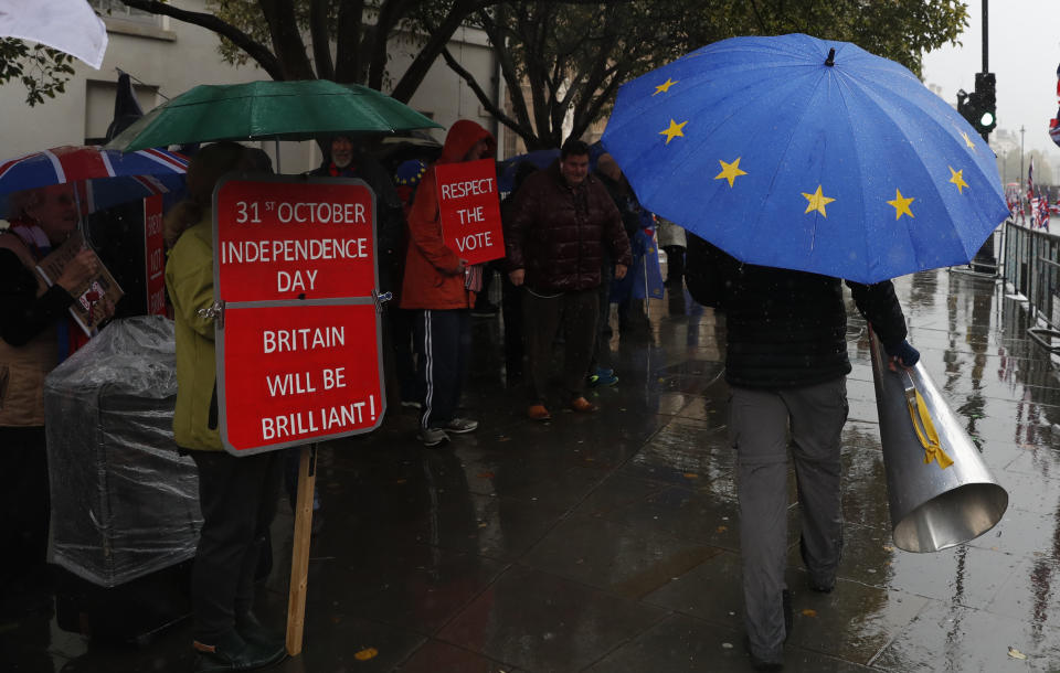 Anti-Brexiteer Steve Bray carries his megaphone past pro Brexit supporters as they shelter from the heavy rain outside the Houses of Parliament in London, Thursday, Oct. 17, 2019. (AP Photo/Alastair Grant)