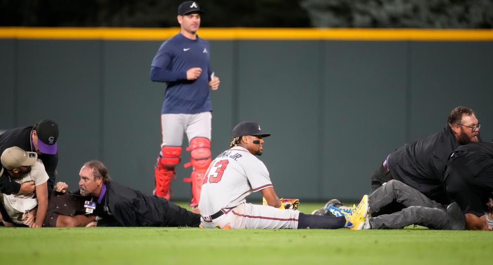 Atlanta Braves right fielder Ronald Acuna Jr., bottom center, ends up on the turf as field guards wrestle down two fans who approached him as he took his spot in the field for the bottom of the seventh inning of a baseball game against the Colorado Rockies, Monday, Aug. 28, 2023, in Denver. (AP Photo/David Zalubowski)