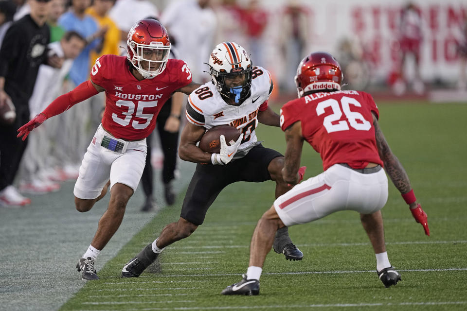 Oklahoma State wide receiver Brennan Presley (80) runs up field after catching a pass as Houston defensive back Dorian Friend (35) and Moses Alexander (26) defend during the second half of an NCAA college football game Saturday, Nov. 18, 2023, in Houston. Oklahoma State won 43-30. (AP Photo/David J. Phillip)