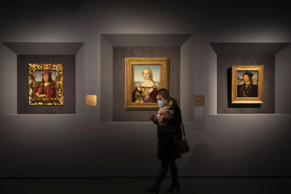 A woman wearing a mask walks past, from left, Raphael's portrait of a Young Man with an Apple, Young Woman with Unicorn and Portrait of a Man, at a press preview of Raphael's exhibition in Rome, Wednesday, March 4, 2020. The paintings, drawings and sketches in the most ambitious assemblage ever of Raphael works in an exhibition, more than even the Renaissance superstar had in his workshop at one time, are collectively insured for 4 billion euros ($.4 billion), against the likes of theft or vandalism. But no money can guarantee that Italy’s outbreak of coronavirus, the largest in Europe, won’t play havoc with the three-month run in Rome of the art world’s eagerly-awaited blockbuster. (AP Photo/Domenico Stinellis)