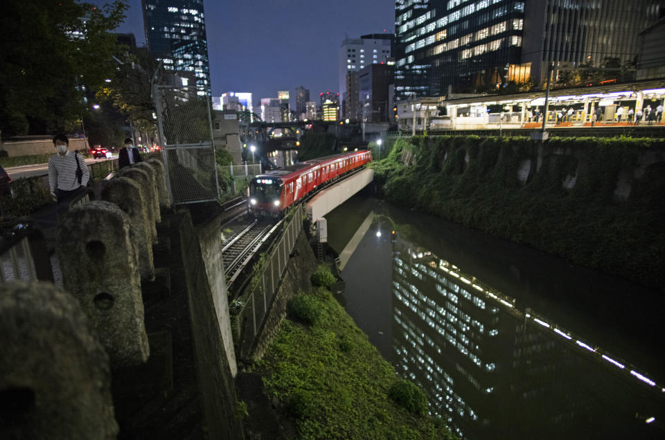 People wearing face masks walk along the Kanda River as a train passes by near a station in Tokyo, Thursday, Sept. 9, 2021. Japan announced Thursday it is extending a coronavirus state of emergency in Tokyo and 18 other areas until the end of September as health care systems remain under severe strain, although new infections have slowed slightly. (AP Photo/Hiro Komae)