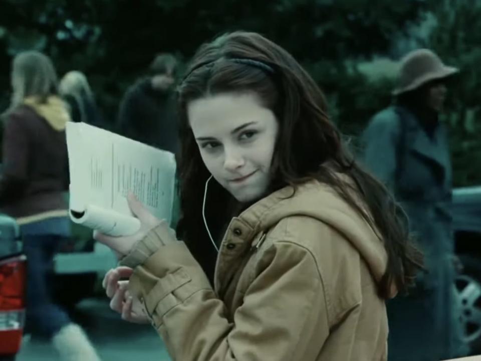 bella leaning against her truck holding up a book in twilight