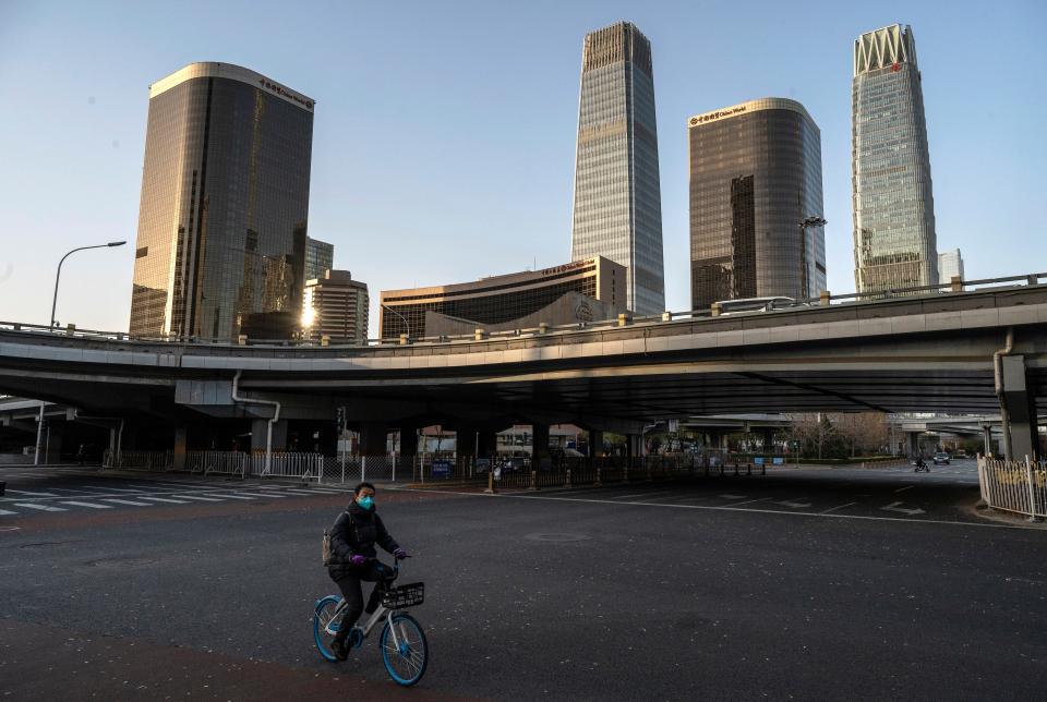 A woman wears a mask to prevent the spread of COVID-19 as she rides a bike across a nearly empty intersection in the Central Business District on November 25, 2022 in Beijing, China.