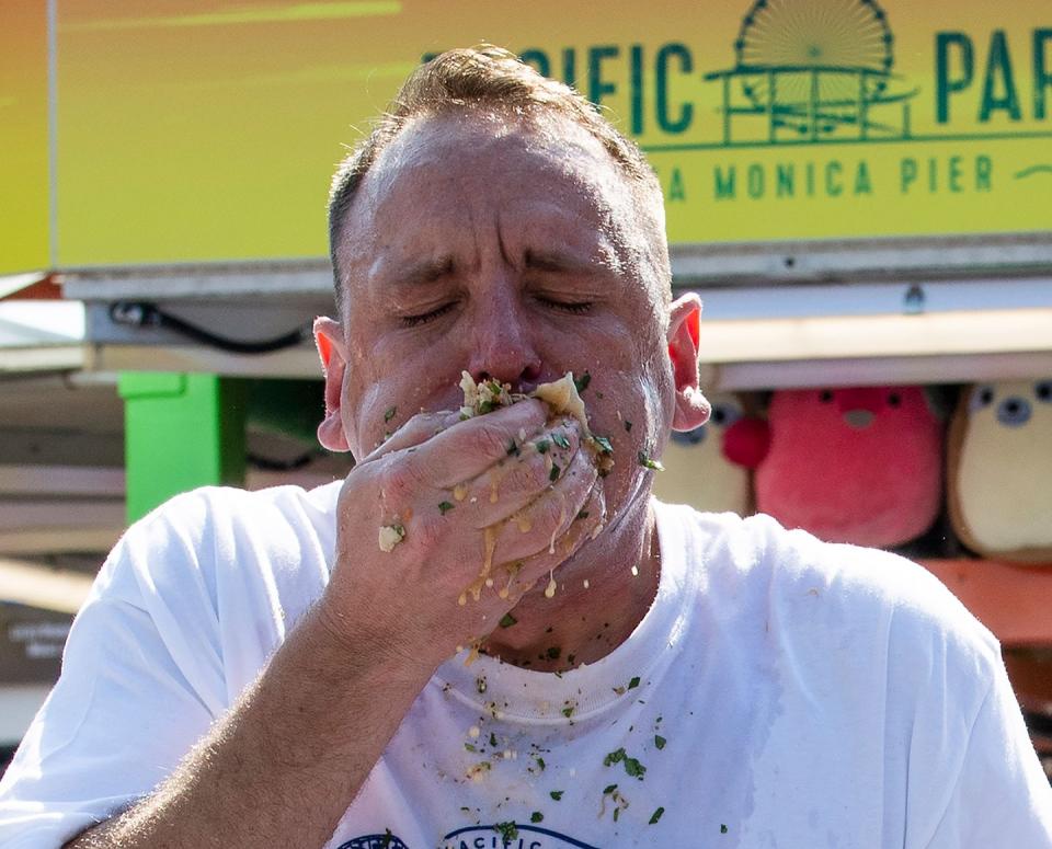 joey chestnut with his eyes closed as he shoves a handful of tacos into his mouth