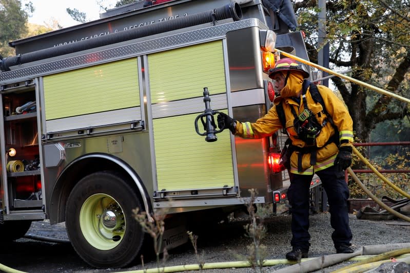 A firefighter passes a hose nozzle while working on a burning structure at the Kincade fire in Calistoga, California