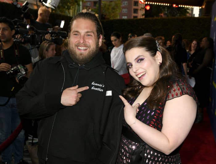 Beanie with Jonah on the red carpet. She wears a short-sleeved black and red dress and he wears a hoodie that reads "beanie's brother" on the lapel