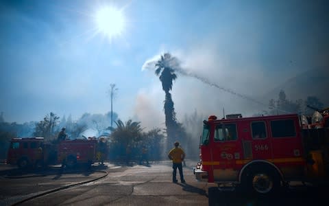 Firefighters water down trees and bushes near homes on Bell Canyon Road in West Hills, near Malibu - Credit: FREDERIC J. BROWN/AFP/Getty Images