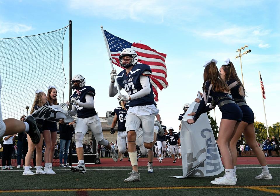 Medway's Sean Anderson carries the American flag as the Mustangs take the field for the home opener against Westwood at Medway High School, Sept. 29, 2022.  