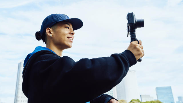 Sony ZV-1 II camera in a vlogger&#39;s hands with blue sky in the background