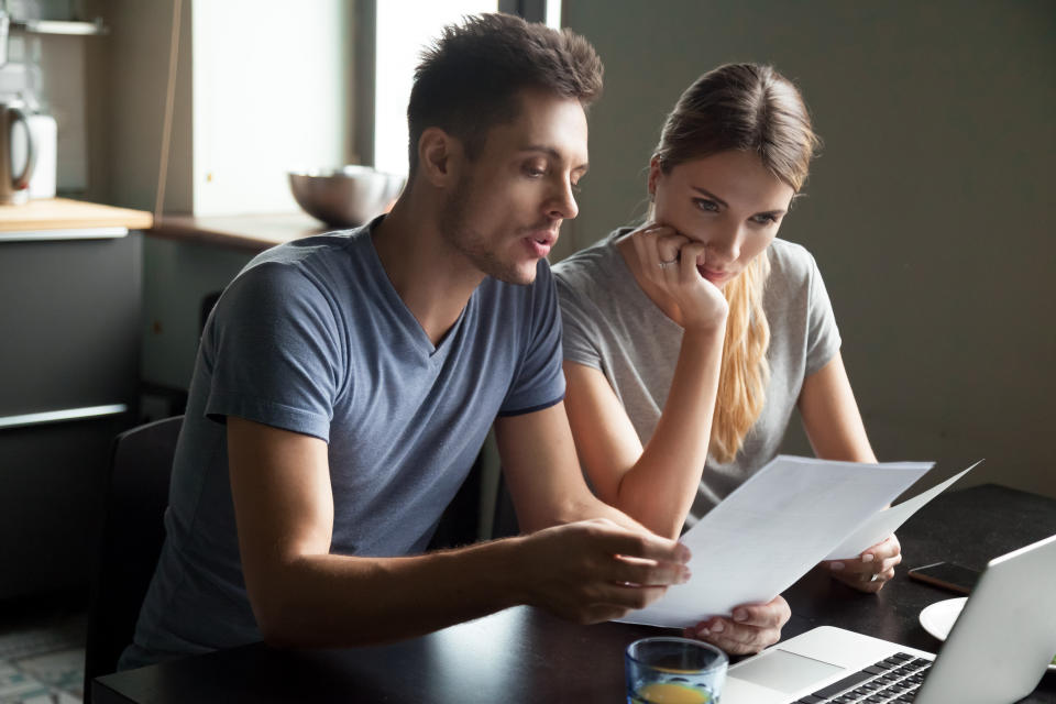 Young couple checking paperwork while sitting at a laptop. 