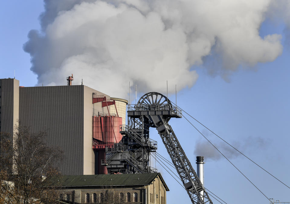 A coal-fired power station steams behind the pit frame of Germany's next to last coal mine in Ibbenbueren, Germany, Tuesday, Dec. 4, 2018. An industrial history will end later this month when the last stone coal mine in Germany will be closed in Bottrop. (AP Photo/Martin Meissner)