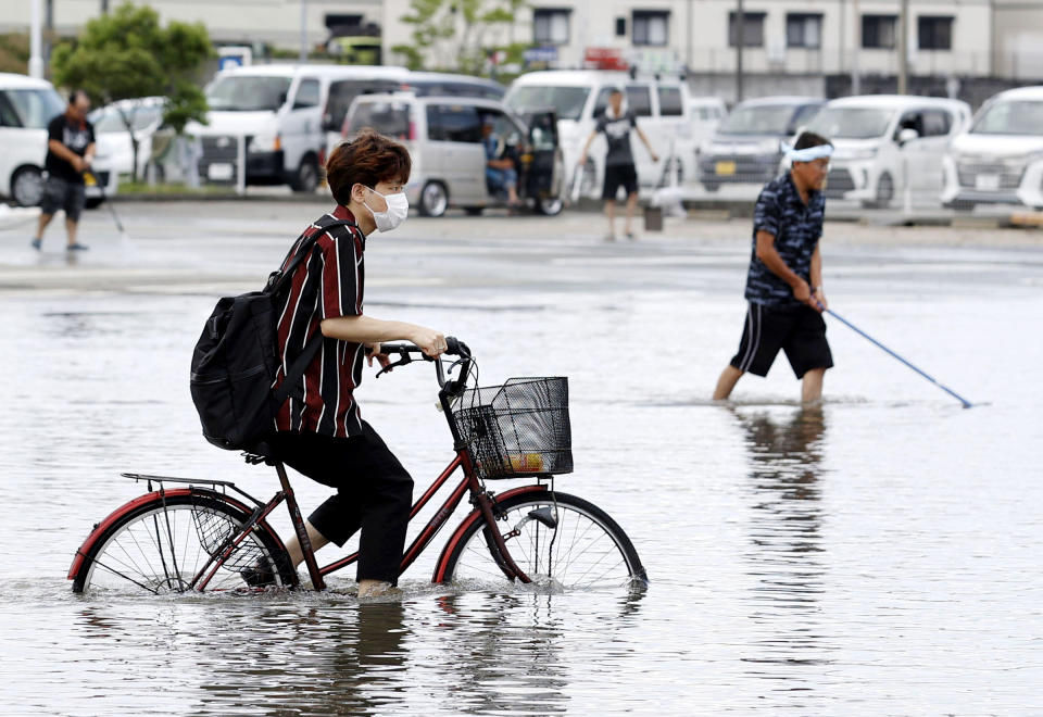 A man on a bicycle makes his way through a flooded road following heavy rains in Kurume, Fukuoka prefecture, southern Japan Wednesday, July 8, 2020. Floodwaters flowed down streets in southern Japanese towns hit by heavy rains. (Shoei Miyano/Kyodo News via AP)