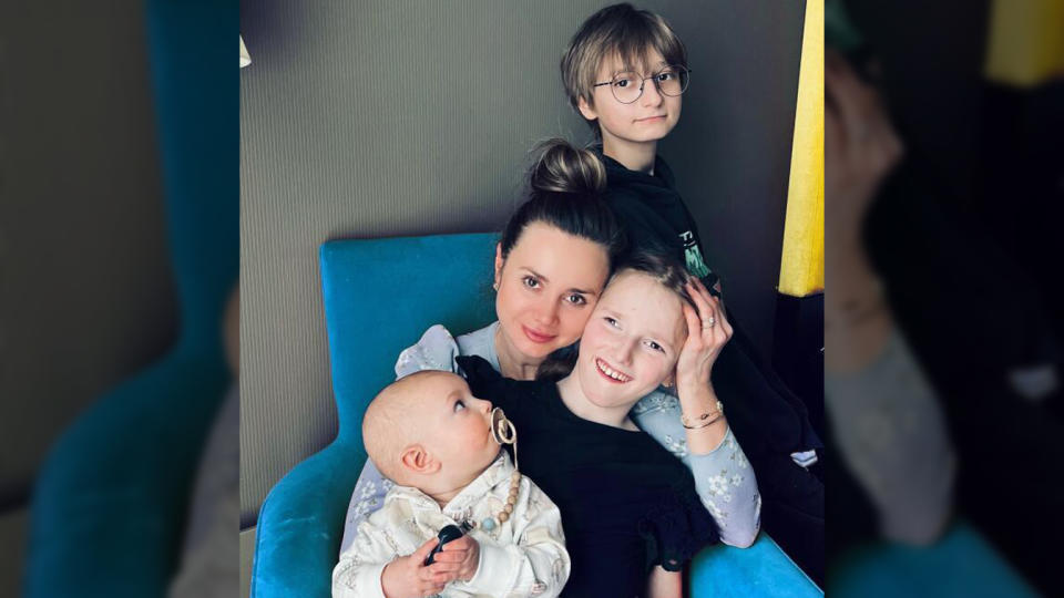 Valeria Skorovohach sits in a chair with two of her children as the third leans against the chair behind her. 